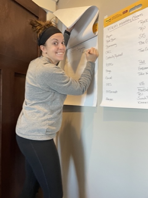 Molly smiling at the camera while writing on a wall-sized paper